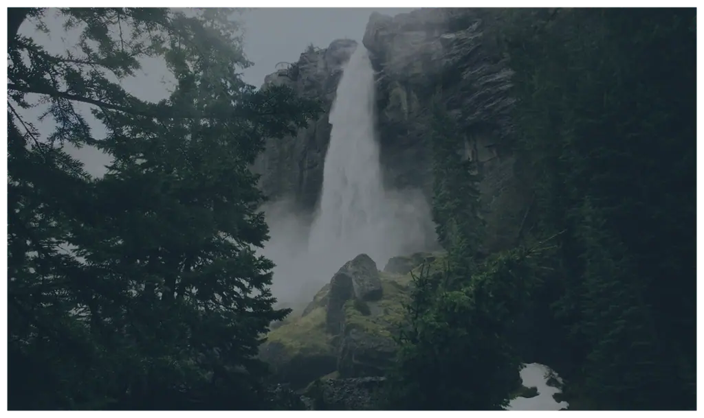 A towering waterfall plunging down a misty cliff face into deep evergreen forest